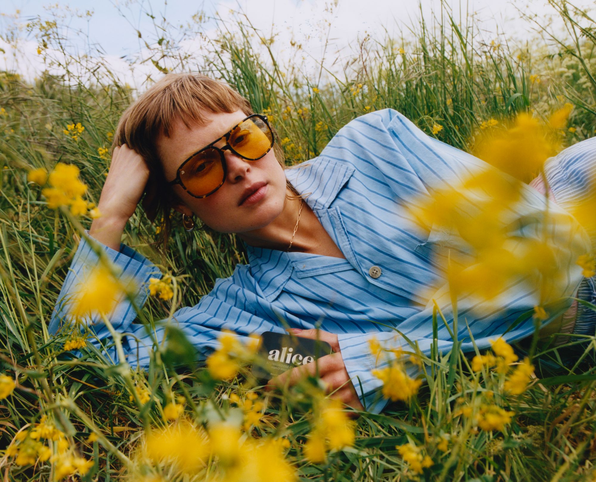 A woman lying in a wildflower meadow, wearing tinted sunglasses