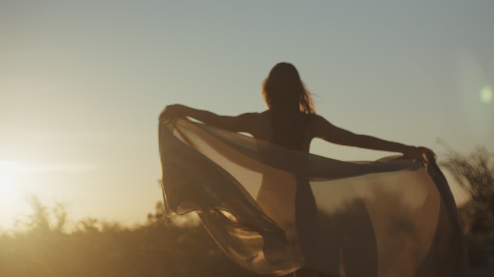 Woman holding a scarf in the wind at sunrise