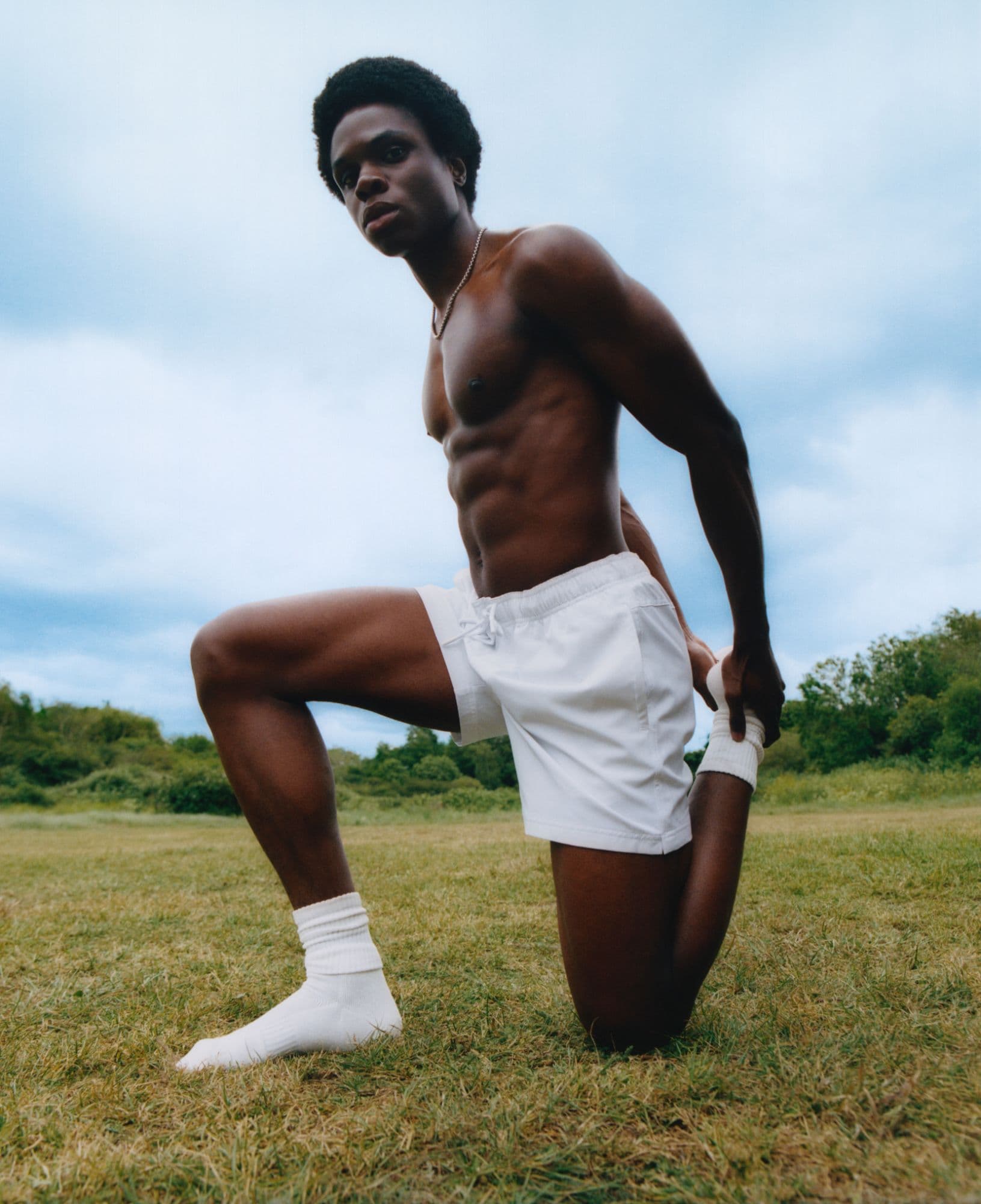A man kneeling on grass in an open field, resting after exercise